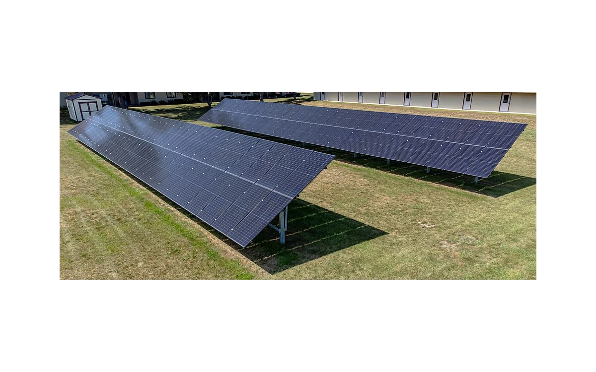 Ground-mounted photovoltaic rows beside grass and buildings, shown in visible light.