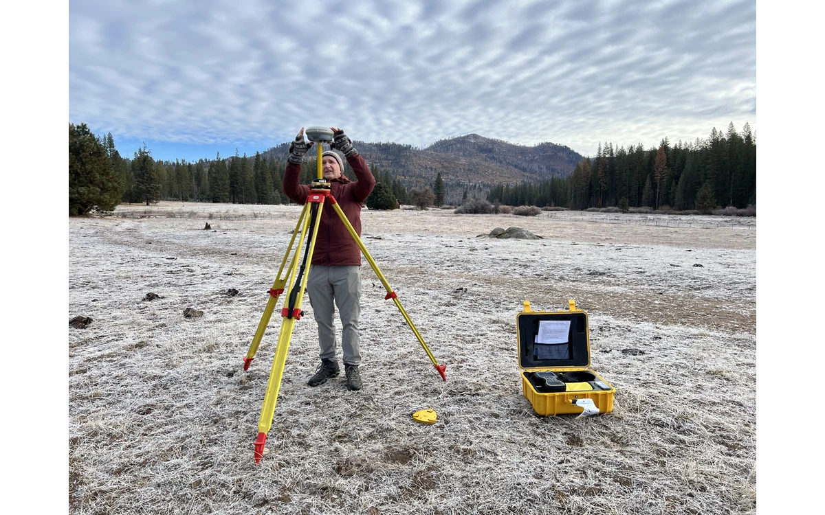 USGS scientist setting up a tripod-mounted GNSS base station in a frosty Yosemite field.